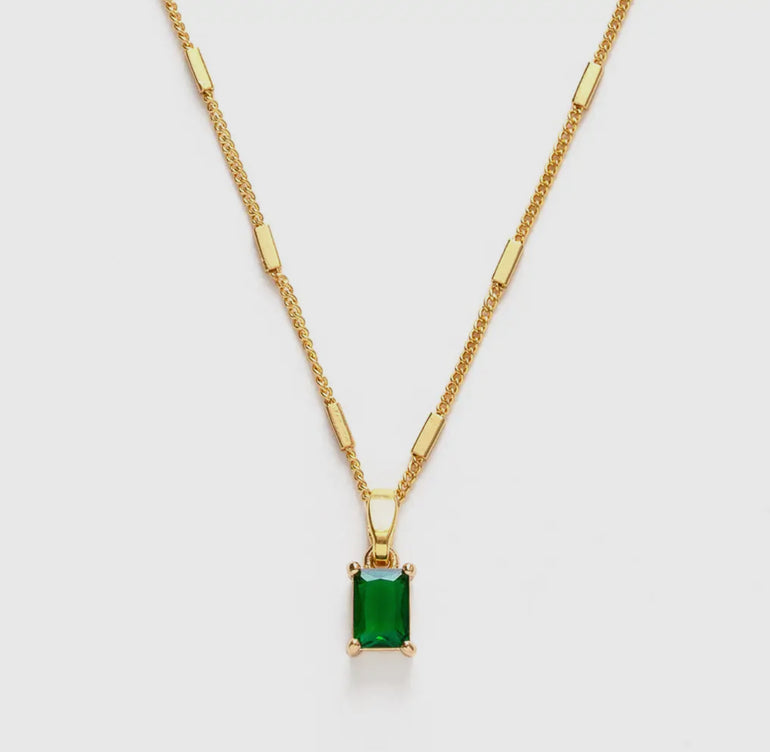 Gold necklace with a green gemstone pendant on a white background