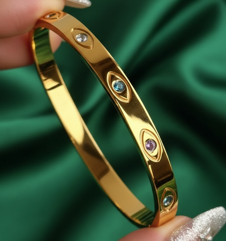 Stay protected and stylish with our Evil Eye Gold Bangle. Made with titanium steel, 18K gold plating, and zircon stones for long-lasting shine. Perfect for daily wear, stacking, and gifting. Shop Latina-owned jewelry at Oreja Linda.