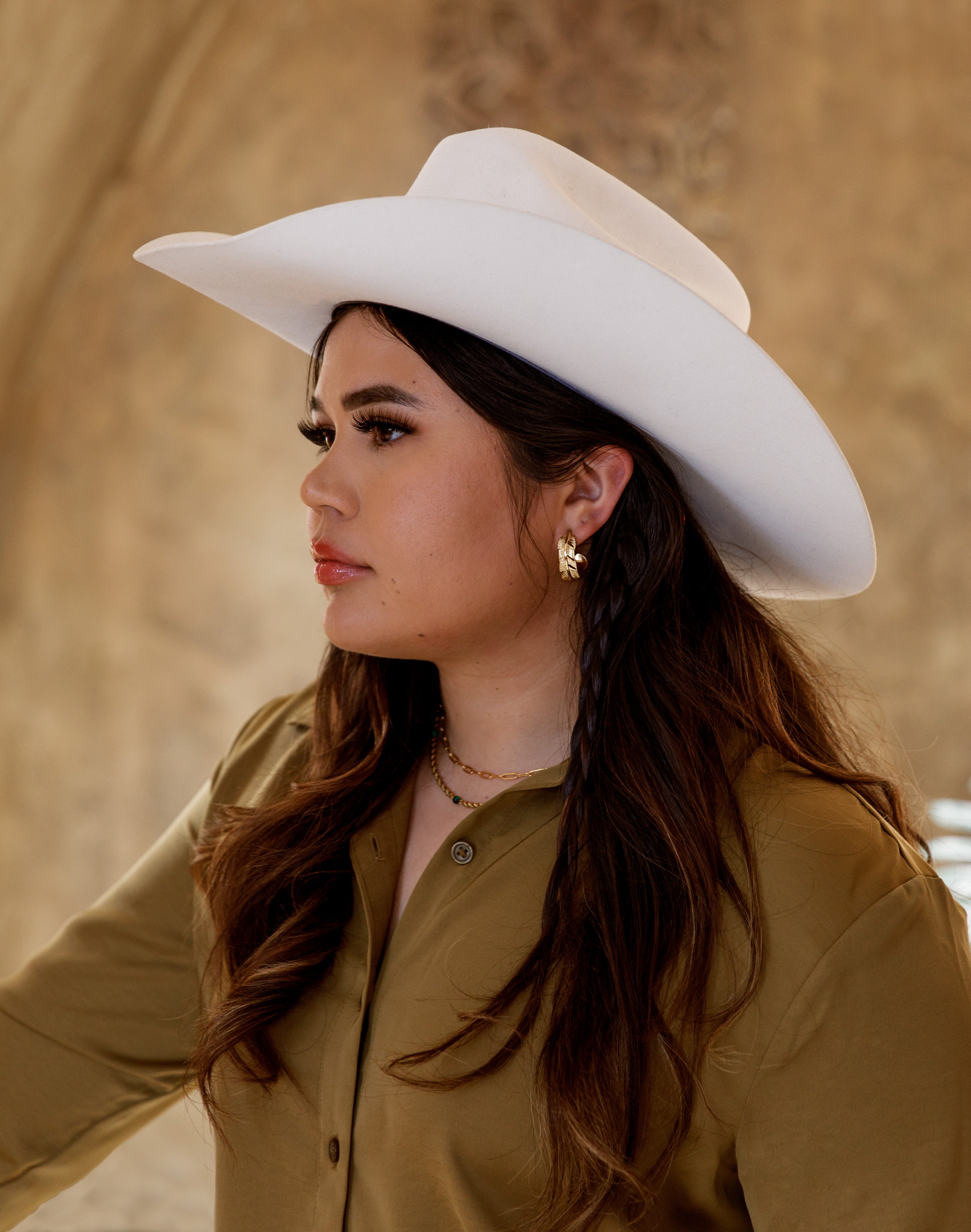 Modern Latina wearing gold hoop earrings and gold chain dainty necklace inspired by the Latino and Hispanic culture and traditions. Wearing green satin shirt to represent her cactus roots and white cowboy hat for her culture and Latina aesthetic