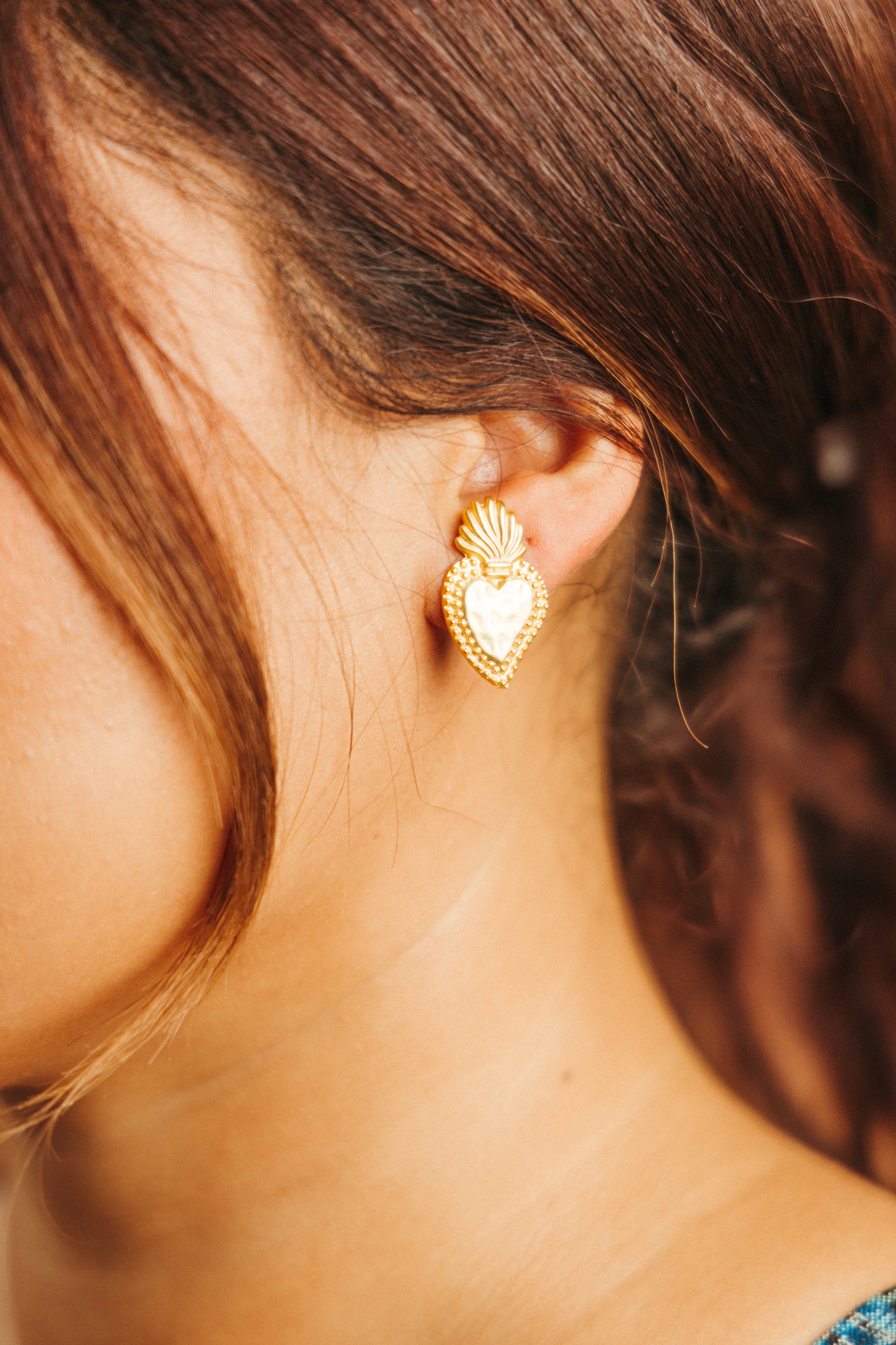 Sacred Heart Latino inspired heart shaped stud gold earrings on a Latina girl with brown skin and brown hair modeling for a Latina small business